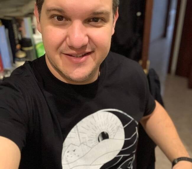 Retrato de Xavier Giner sonriente, en fondo de estantería y con camiseta de diseño lunar y espacial.